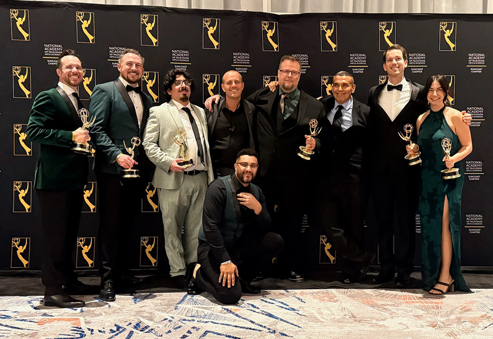 InEd Studios team members stand in front of Emmy background in group smiling holding emmys