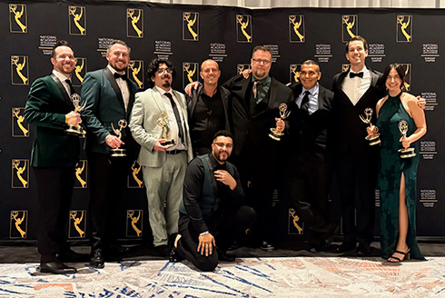 InEd Studios team members stand in front of Emmy background in group smiling holding emmys
