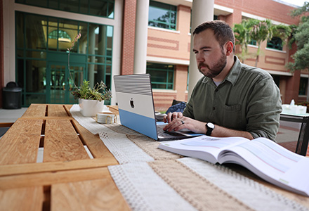 student jacob sits at table using a laptop