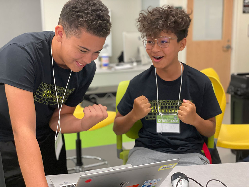 Two middle school students celebrate a success as they compete with other teams in cybersecurity challenges at summer camp.