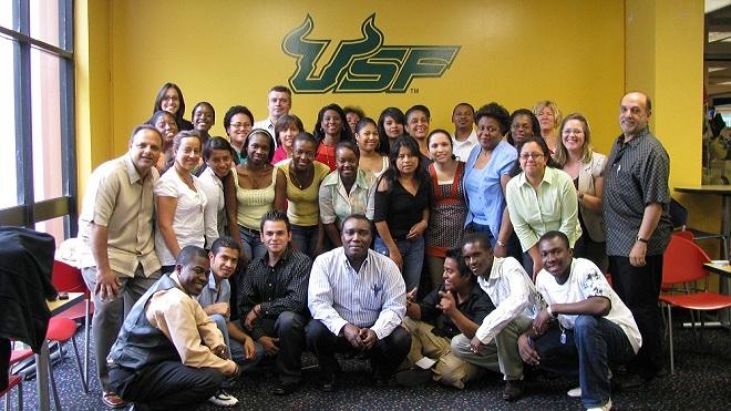 Group of USF students take a picture in front of a yellow wall with the USF logo.