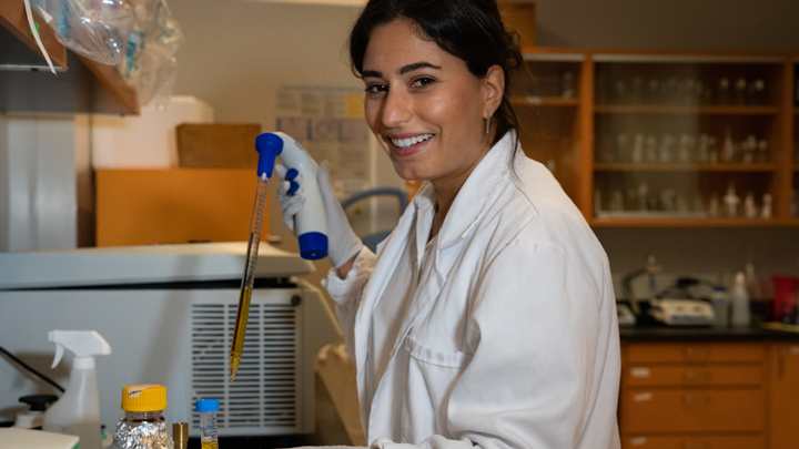 Kema Malki smiling in the lab holding lab equipment