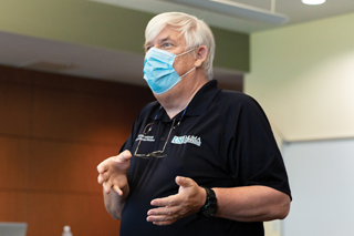 Grandon Gills giving a lecture in a blue mask