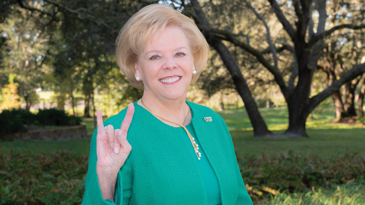 Portrait of USF President Rhea F. Law flashing the bull-horn hand singal, on the Tampa campus, in an aqua suit.