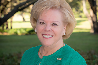 A smiling USF President Rhea F. Law pictured outdoors, surrounded by oak trees, on the Tampa campus.