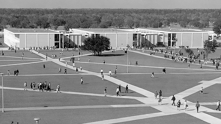 A black and white aerial photo of students walking across the Tampa campus, a view of the College of The Arts buildings in the background, sidewalks making a lattice across the plaza, circa 1966.