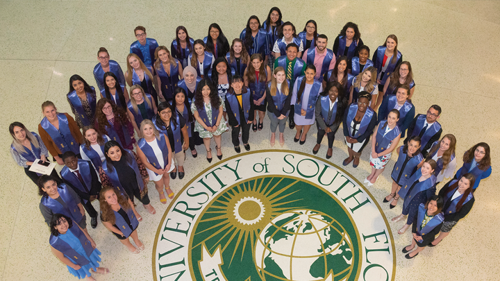 View from above of the first USF Phi Beta Kappa membership class with blue stoles, posed around the USF seal.