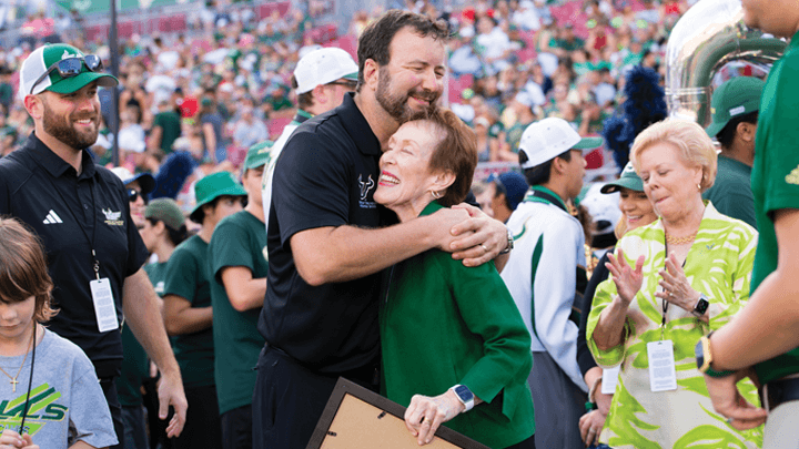 Former USF President Betty Castor and former HOT band director Matthew McCutcheon share a hug on the field at Raymond James stadium.