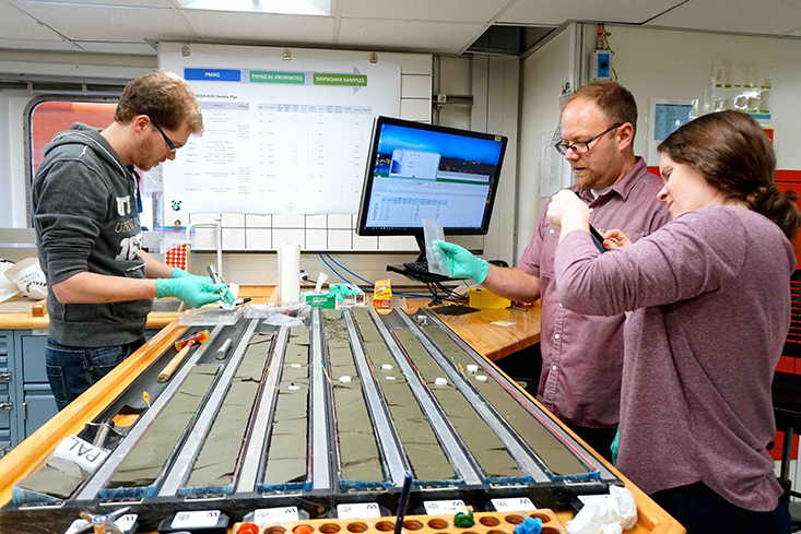 PhD candidate, Imogen Browne, samples sediment with fellow scientists on board International Ocean Discovery Program (IODP) Expedition 374 to the Ross Sea in 2018. Photo courtesy of IODP.