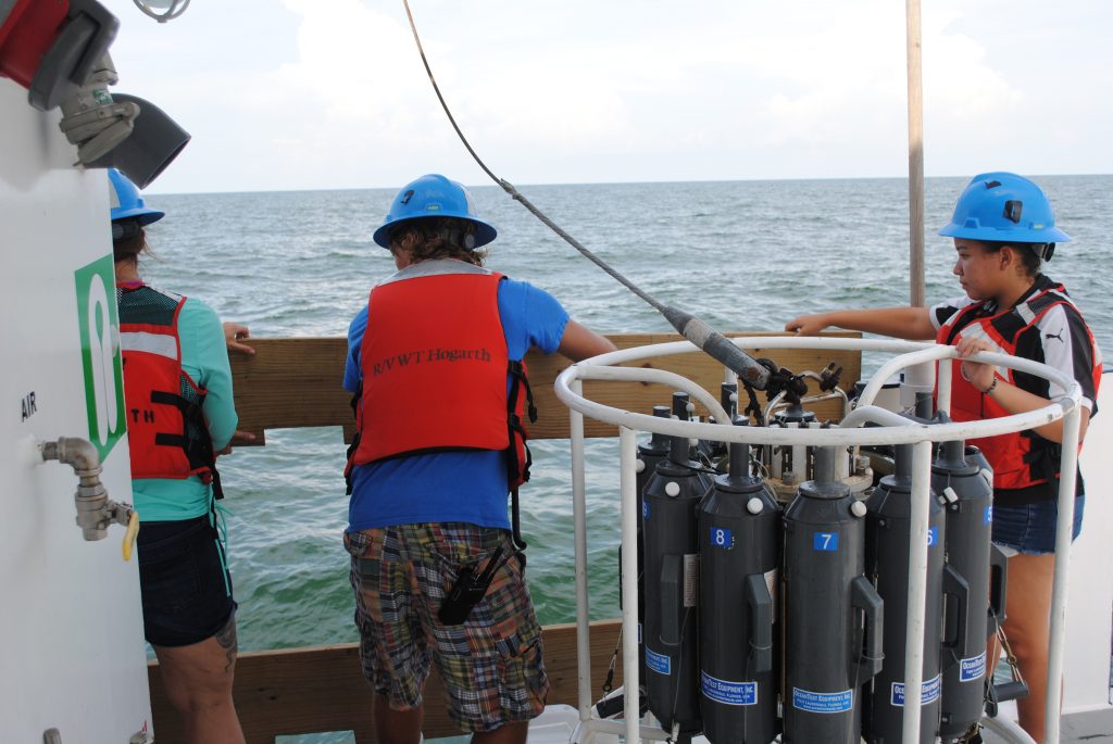 In addition to her primary role of data recorder on the midnight to noon shift, Andrea Rodriguez Campos (holding the CTD rosette) is shown here assisting with a CTD cast over the Desoto Canyon.