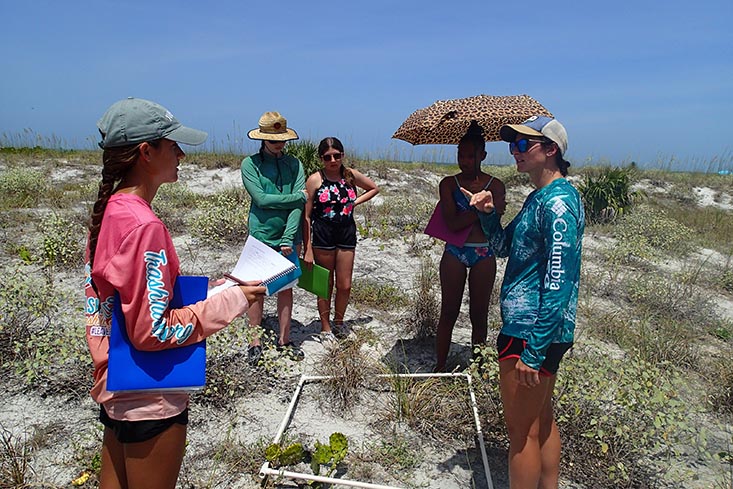 Science mentor Kylee Rullo shows campers how to measure the percent cover of vegetation within the dune swale.
