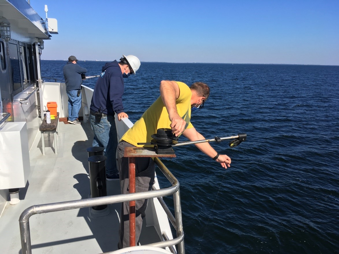 Eddie Hughes, Co-Chief Scientist (background, left), and Andrew Warren, FIO Ship Operations, do a bit of puppeteering of the wires holding the calibration sphere while Captain Brendon Baumeister looks on.