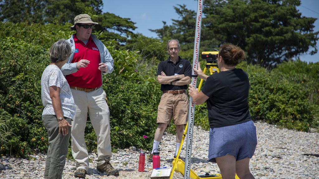 Gregory Berman demonstrates beach profiling to experienced journalists from the Woods Hole Oceanographic Institution's Ocean Science Journalism program. Berman explains how beaches change over time and how projected changes in sea level may shift future shorelines. Courtesy of Gregory Berman.