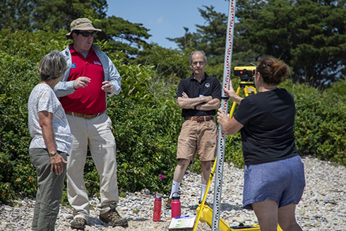 Gregory Berman demonstrates beach profiling to experienced journalists from the Woods Hole Oceanographic Institution's Ocean Science Journalism program. Berman explains how beaches change over time and how projected changes in sea level may shift future shorelines. Courtesy of Gregory Berman.