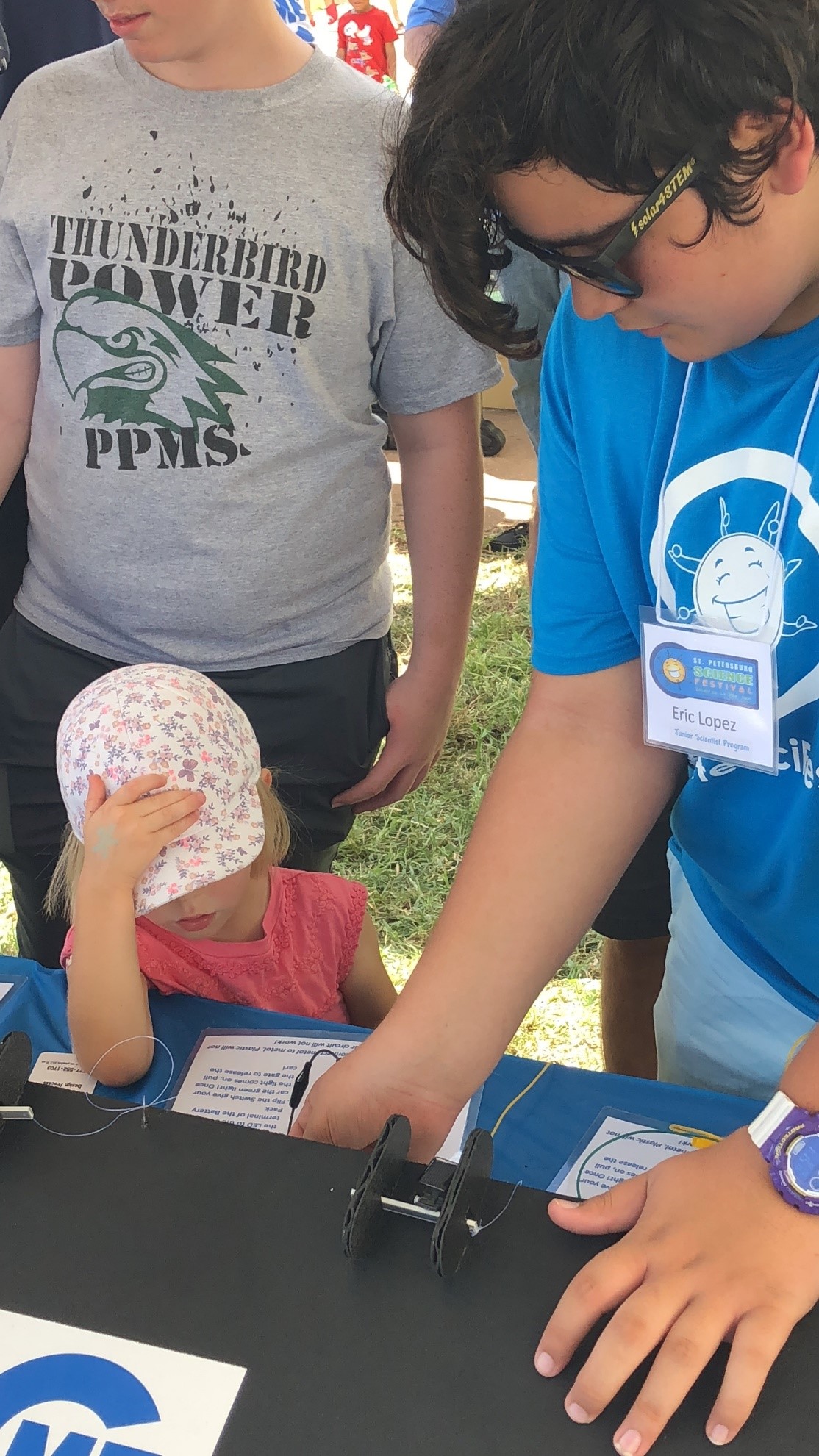 Junior Scientist, Eric Lopez, helps a young festival-goer at the Solar Car Race booth.