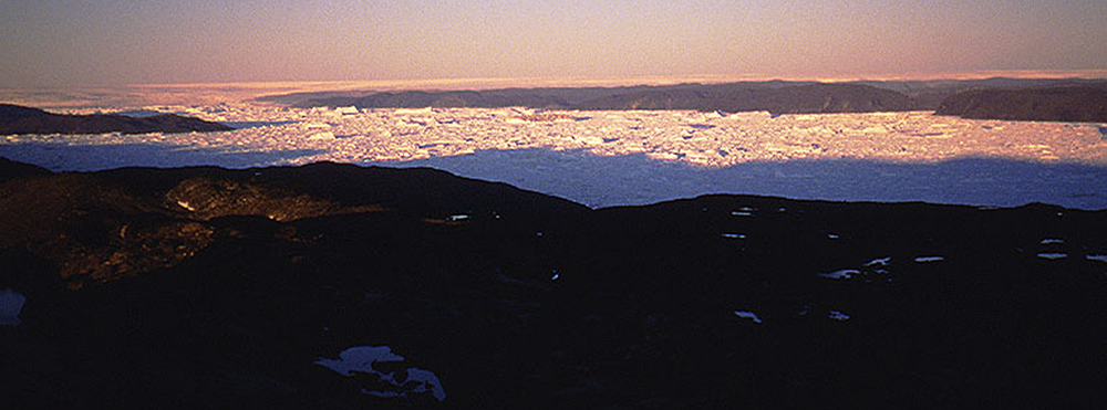 A midnight view of the Greenland Ice Sheet near Ilulissat in July 1991. The background shows the vast ice sheet, while the foreground fjord is choked with icebergs released by one of the world’s fastest-moving outlet glaciers. During the last ice age, this ice sheet was directly connected to the ice masses that covered most of Canada. Credit: Torbjörn Törnqvist