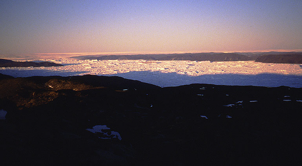 A midnight view of the Greenland Ice Sheet near Ilulissat in July 1991. The background shows the vast ice sheet, while the foreground fjord is choked with icebergs released by one of the world’s fastest-moving outlet glaciers. During the last ice age, this ice sheet was directly connected to the ice masses that covered most of Canada. Credit: Torbjörn Törnqvist