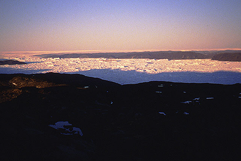 A midnight view of the Greenland Ice Sheet near Ilulissat in July 1991. The background shows the vast ice sheet, while the foreground fjord is choked with icebergs released by one of the world’s fastest-moving outlet glaciers. During the last ice age, this ice sheet was directly connected to the ice masses that covered most of Canada. Credit: Torbjörn Törnqvist
