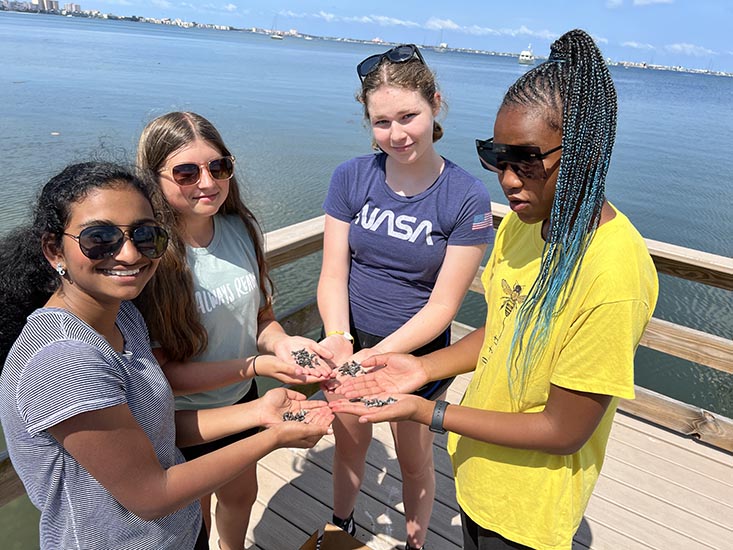 Campers Serah, Ella, Guinnie, and Bri holding shark teeth.