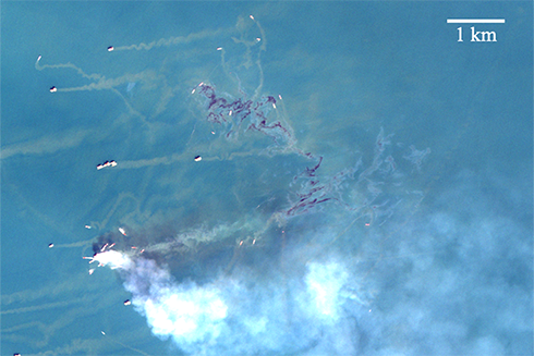 Oil spill from a fire-damaged platform, captured by the Sentinel-2 satellite of the European Space Agency. Fire smoke appears white, while oil slicks appear dark (crude and emulsified oil) or metallic color (oil sheen). Credit: Sentinel-2 data from Copernicus operated by the European Union Agency for the Space Programme in partnership with the European Space Agency. Image generated by Chuanmin Hu of University of South Florida.