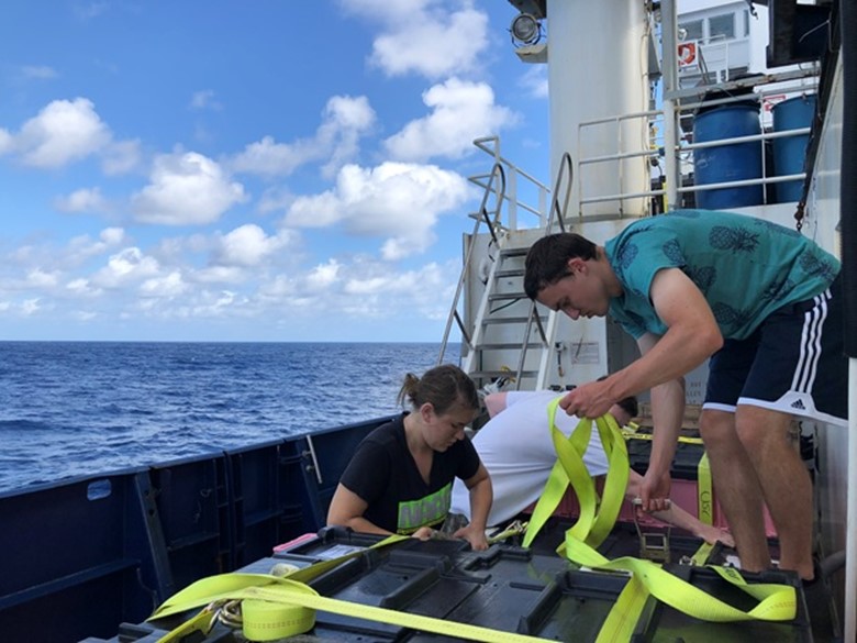 Laramie Jensen (left) and Brent Summers (right) shuffle crates full of seawater samples on deck in preparation for the equatorial Super Station. Image: Alex Fox
