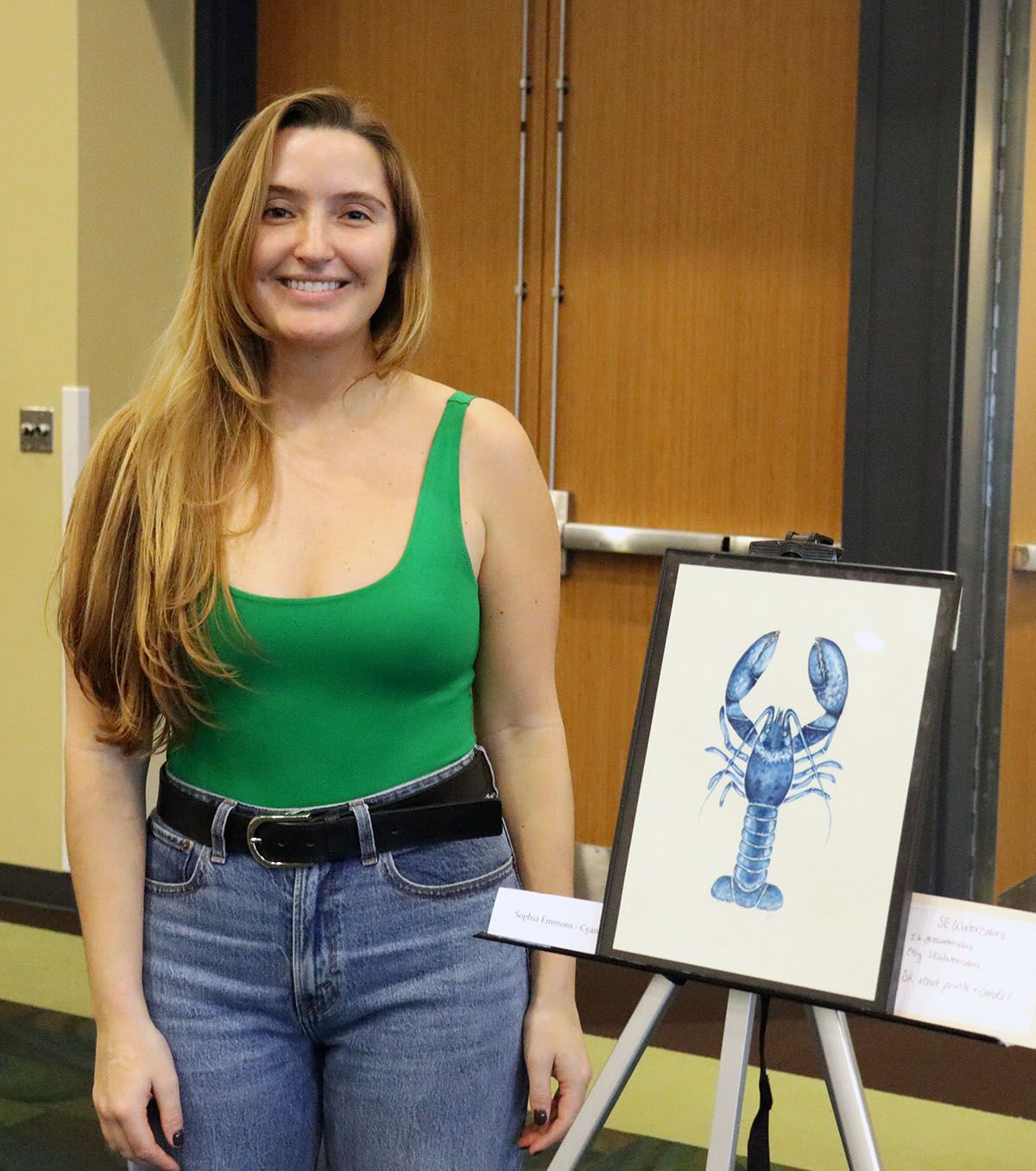 CMS grad student Sophia Emmons next to her watercolor painting titled “Cyan.” PHOTO CREDIT: Makenzie Kerr.