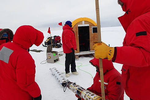 The SCINI ROV (in foreground) is being tested by a researcher prior to deployment, while the acoustic towed package is the white cylinder laying on the snow behind it. The Conestoga wagon “dry lab” is in the background. Photo credit: Stacy Kim.