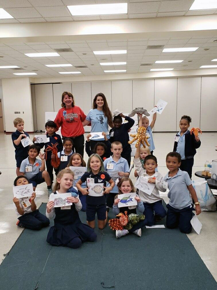 Tricia Burrows (Makenzie’s aunt) and Makenzie Kerr with a first grade class. They are holding up the fish coloring pages they got by deciphering which fish their egg was from.