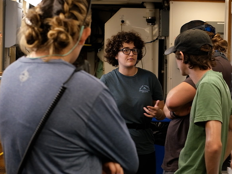 Lilly Verrill (middle) explains the water sample collection process to Sam D'Angelo (left), Sam Elder (front-right), and Orion Witmer (back-right). Photo: Sophie Theiss.