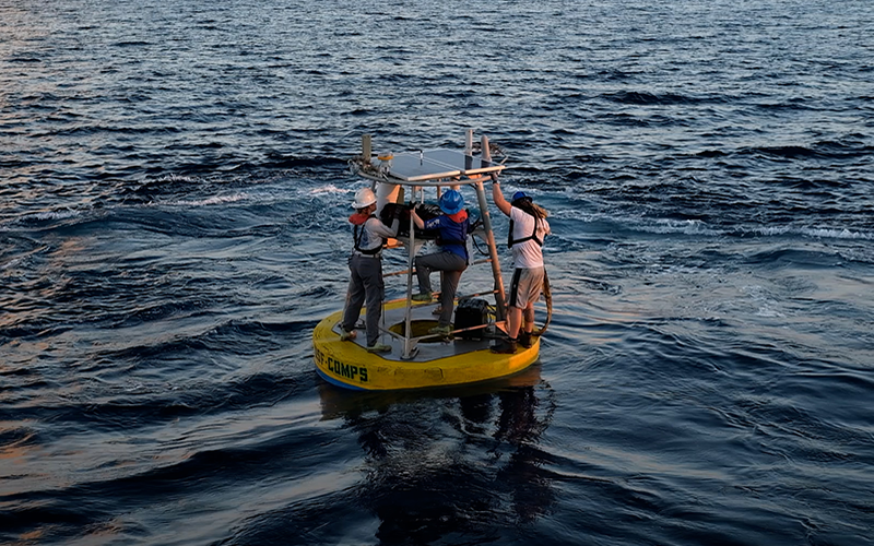 Undergraduate students Sam D’Angelo (left), Grace Humphrey (middle), and graduate student Orion Witmer (right) aboard a buoy working on equipment. Photo: Sophie Theiss.