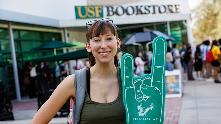 Student standing outside of the Tampa Bookstore, holding a"Horns Up" foam hand