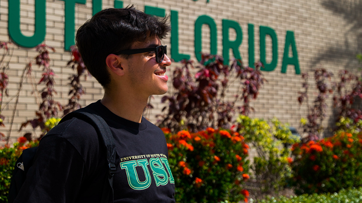 Student wearing sunglasses smiling in front of a University of South Florida sign