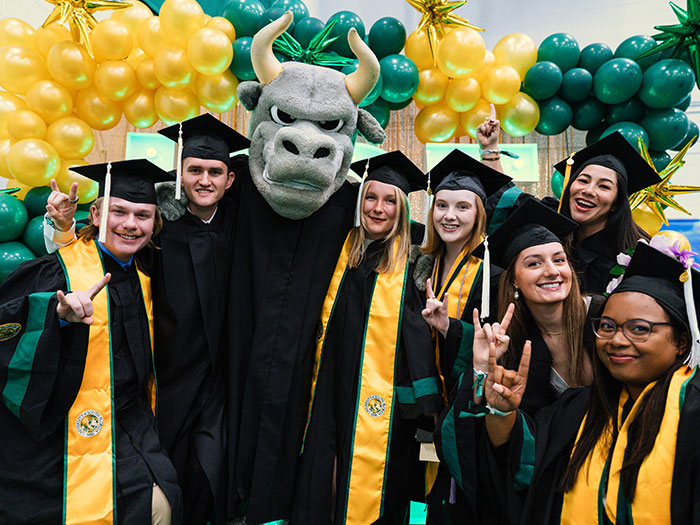 Graduates in caps and gowns pose with Rocky the Bull mascot.