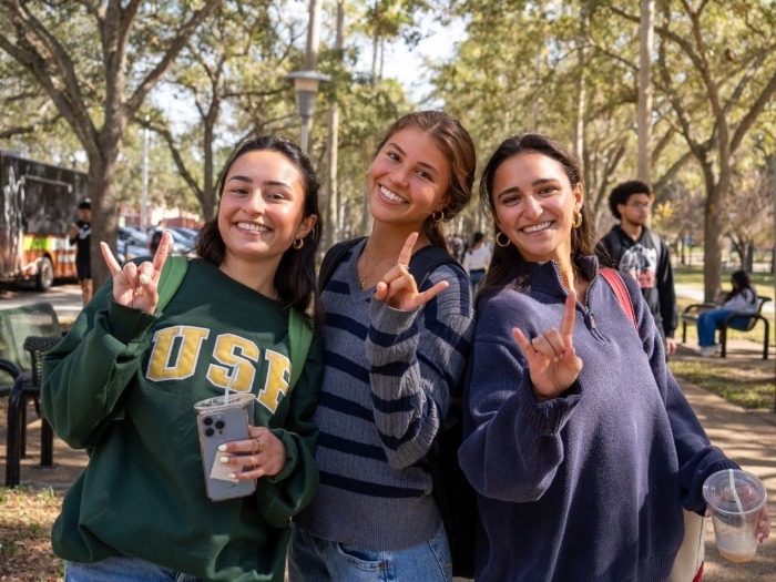 Three students smiling and doing Go Bulls hand gestures.