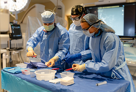 Surgeons stand over table with catheter