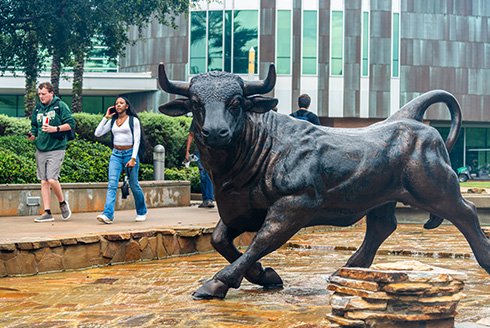 Students walk near the bull statue holding cell phones