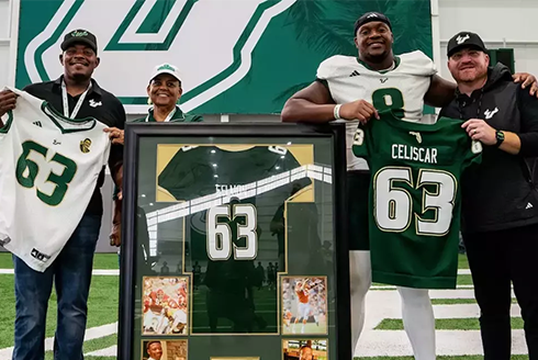 Football players stand with Coach Alex Golesh with Lee Roy Selmon jersey in frame