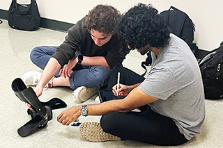 Two students sit, working on medical device