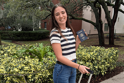 Woman stands on USF campus holding a passport