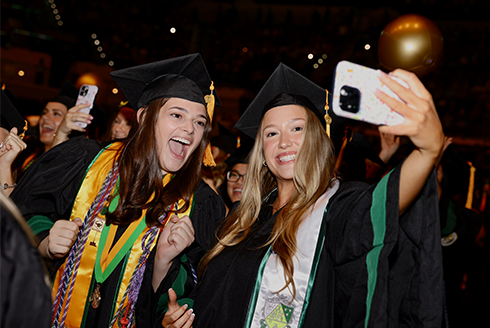 Two students celebrate taking a selfie at USF commencement