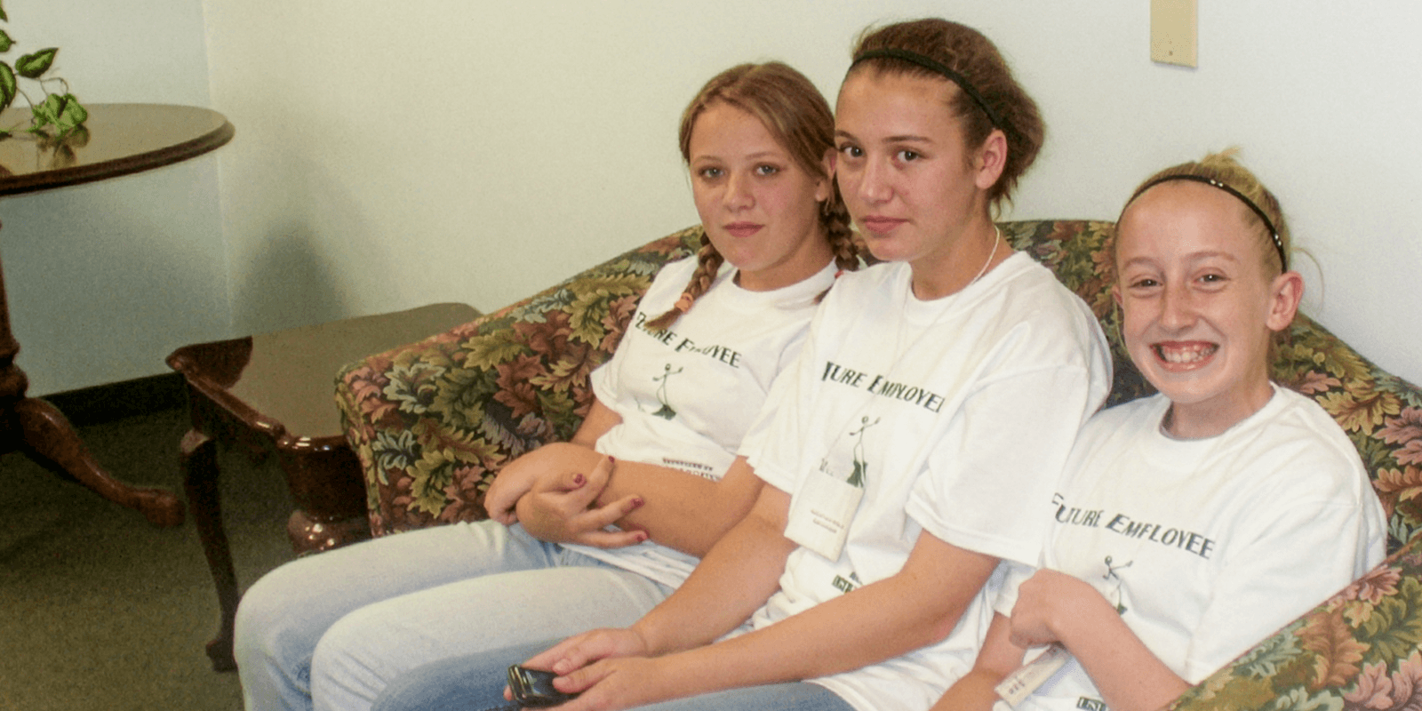 Three girls sit on a couch wearing "Future Employee" T-shirts
