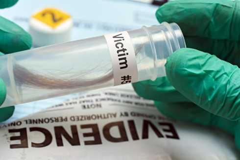 A gloved hand inserts a sample of hair into an evidence collection tube.