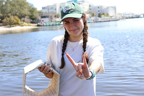Student gives the go bulls hand signal near the water