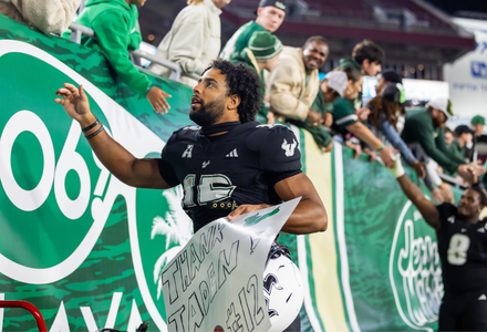 Football player reaches up to greet fans after a game while holder a sign that says "thank you"
