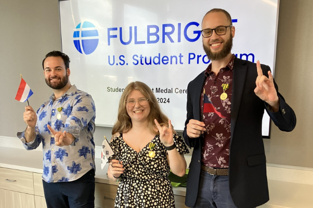 Three Fulbright recipients holding the flags of the countries they will travel to and holding up the go bulls hand sign