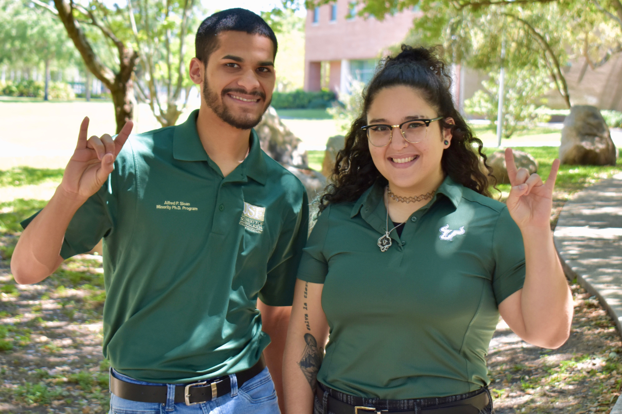 Two students smiling at the camera with the Horns Up hand sign.