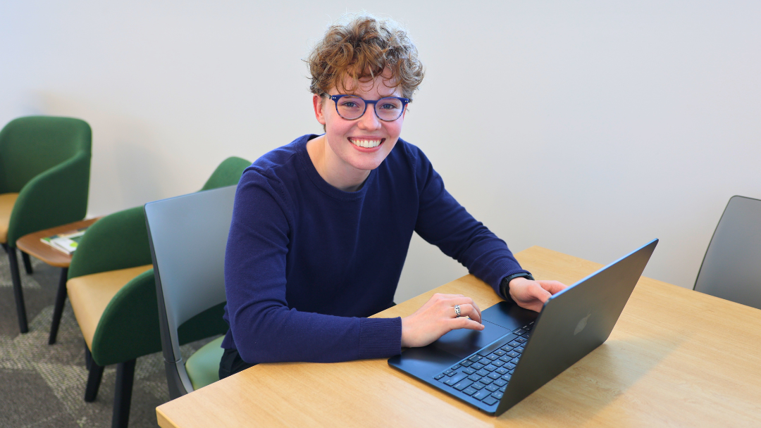 Student sitting at a table on laptop smiling at camera