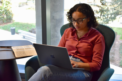 USF student Avani Sanghvi sits in a modern-design chair, focused on a laptop resting on her lap.