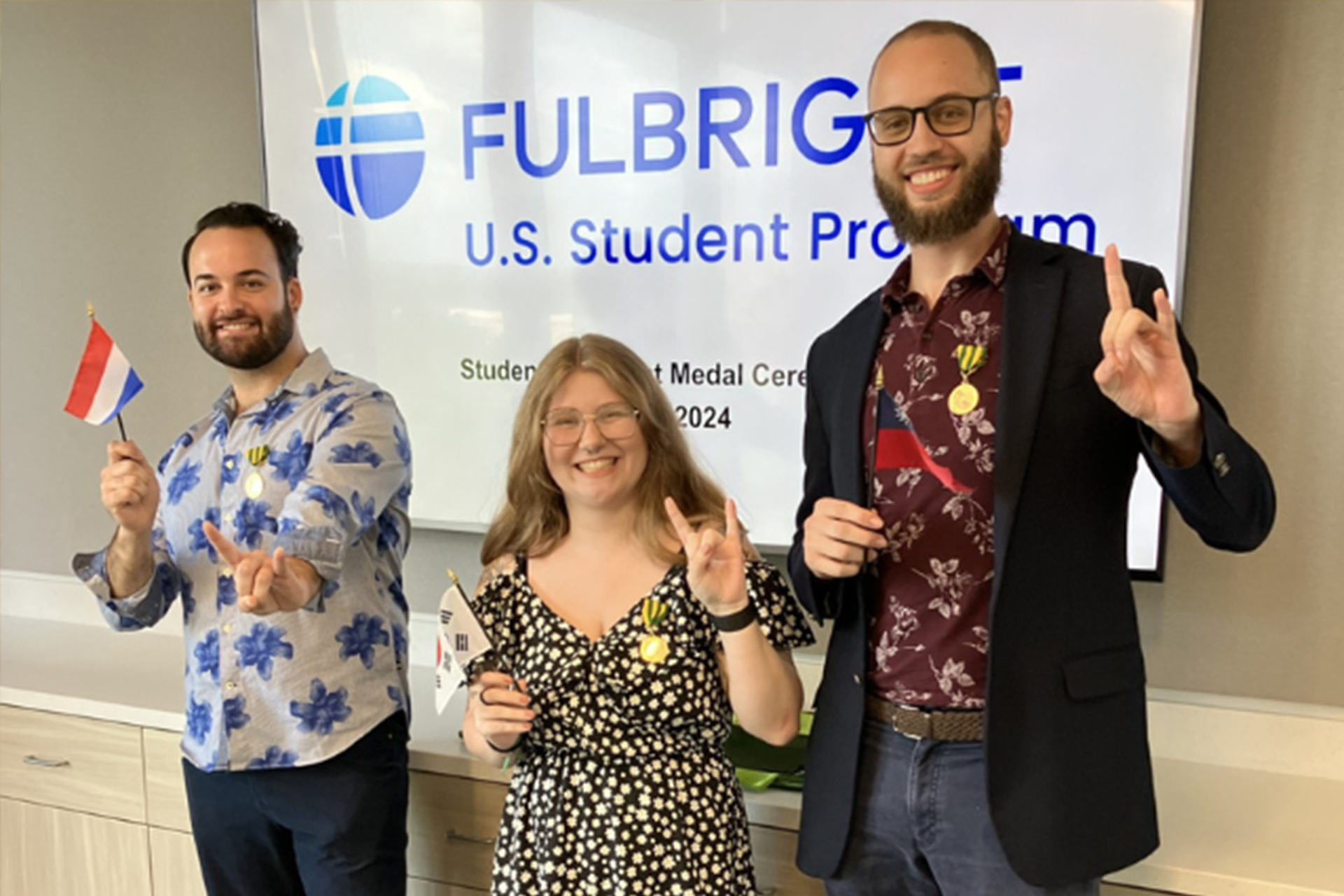 Three Fulbright recipients holding flags