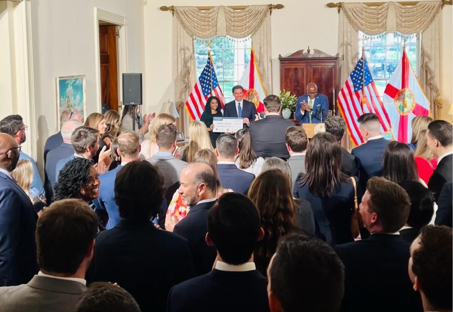 Keerthana Kallarackal receives an award in a crowded government room from Governor Ron Desantis